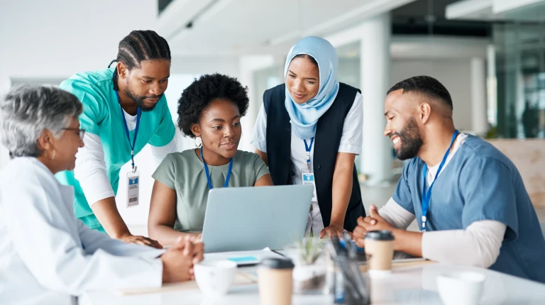 A diverse group of healthcare workers sitting around a computer and smiling.