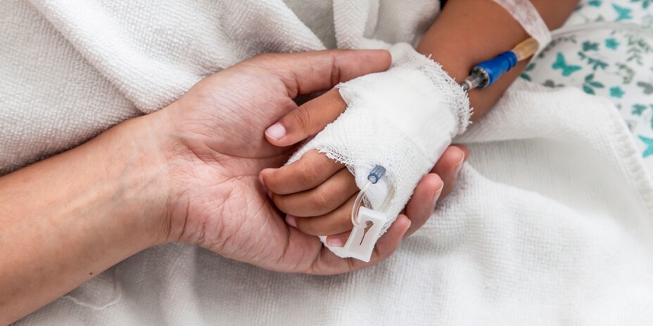 Hand holding a child's bandaged hand with IV tube in place