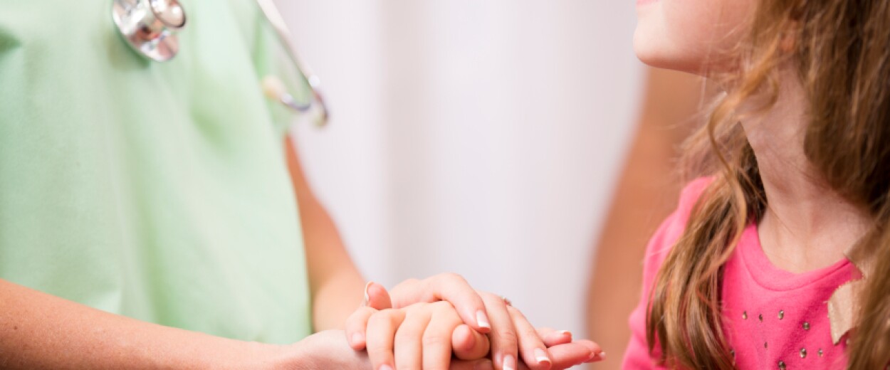 Female nurse in scrubs patting the hand of a young female patient