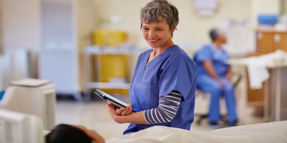 Female nurse in scrubs smiling and talking to patient on hospital bed