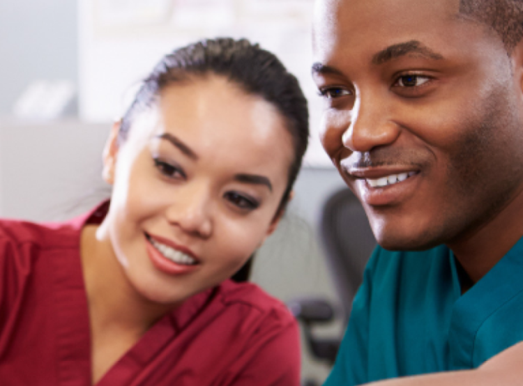 Male and female nurse in scrubs smiling while looking at computer