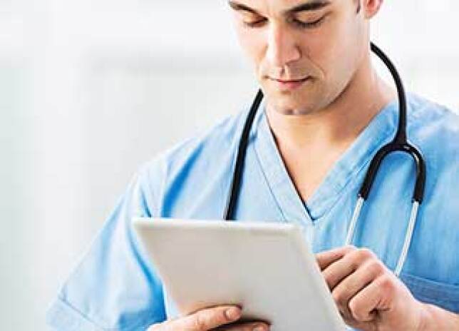 Male nurse in scrubs typing on a tablet