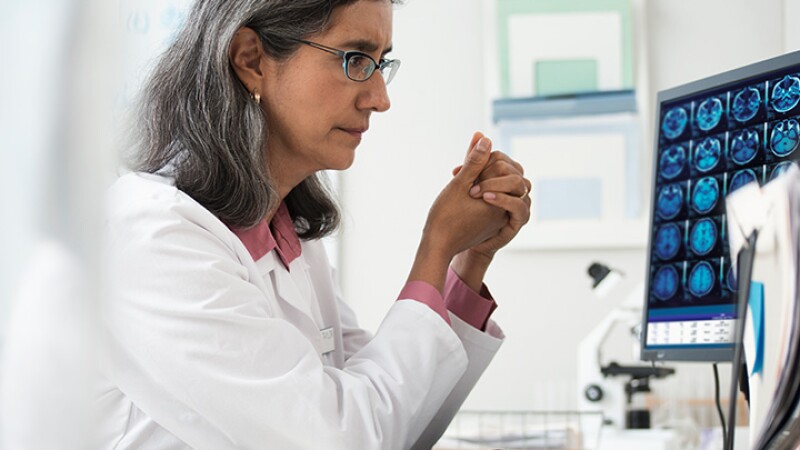 Female medical personnel in lab coat looking at computer screen of brain scans