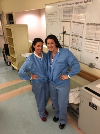 Two female nurses smiling in protective smocks in hospital corridor