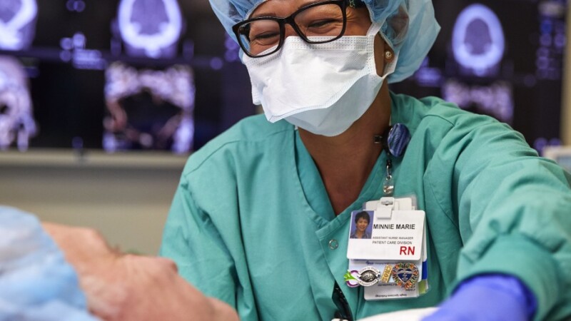 Nurse in scrubs smiling over a patient in a hospital setting