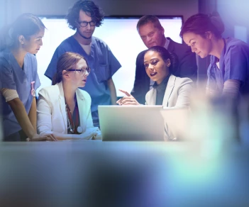 Team of nurses grouped together looking over something being shared on a laptop screen