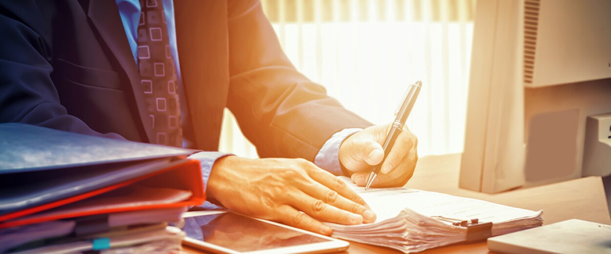 Close up of a man in a suit and tie writing on papers with a pen