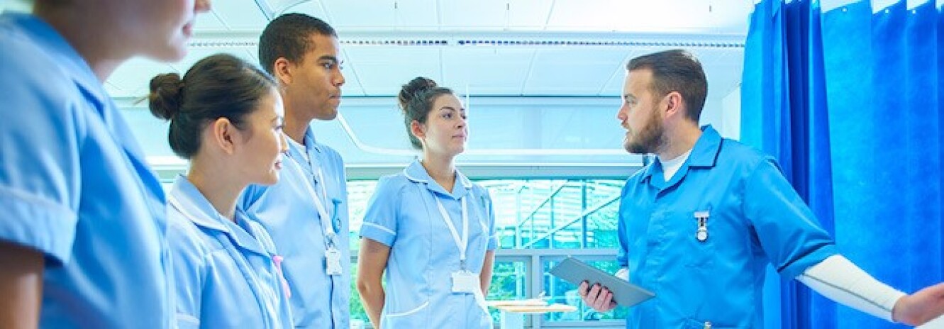 Male nurse in scrubs holding tablet explaining something to a group of nurses in scrubs