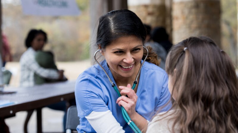 Volunteer nurse smiles while checking young girl at park clinic