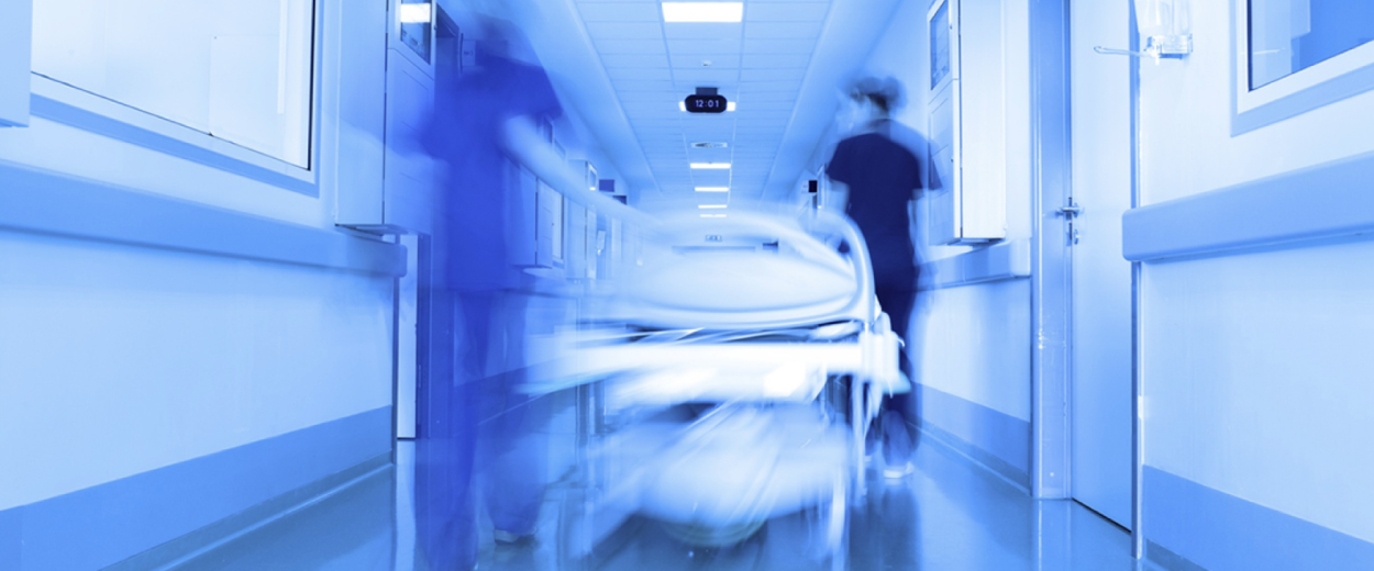 Two nurses in scrubs rushing a gurney down a hospital corridor