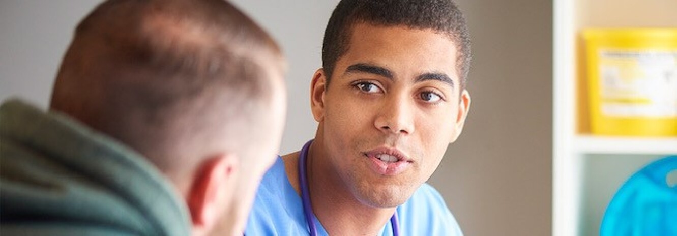 Male nurse in scrubs speaking to male patient whose back is to camera