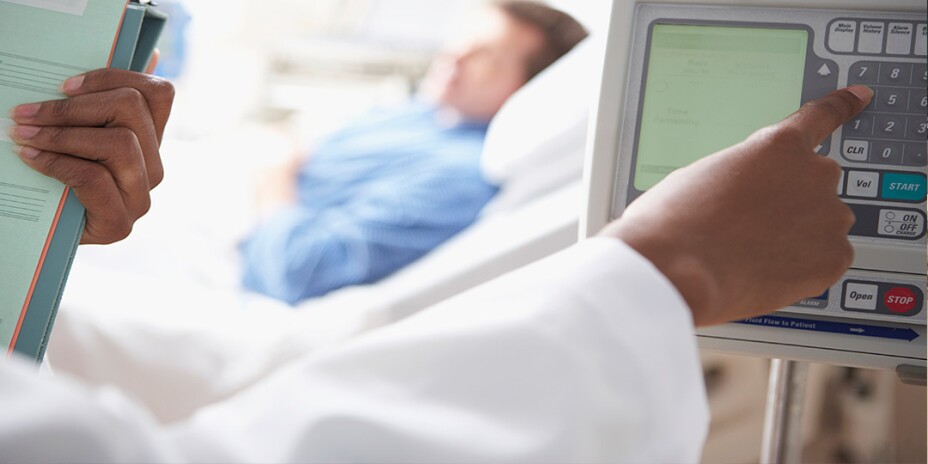 Close up of medical personnel typing numbers in on a monitor with a male patient in hospital bed in background