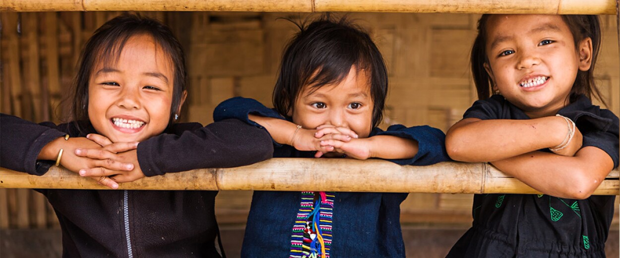 Three small children smiling with their arms crossed in front of them on a bamboo stand