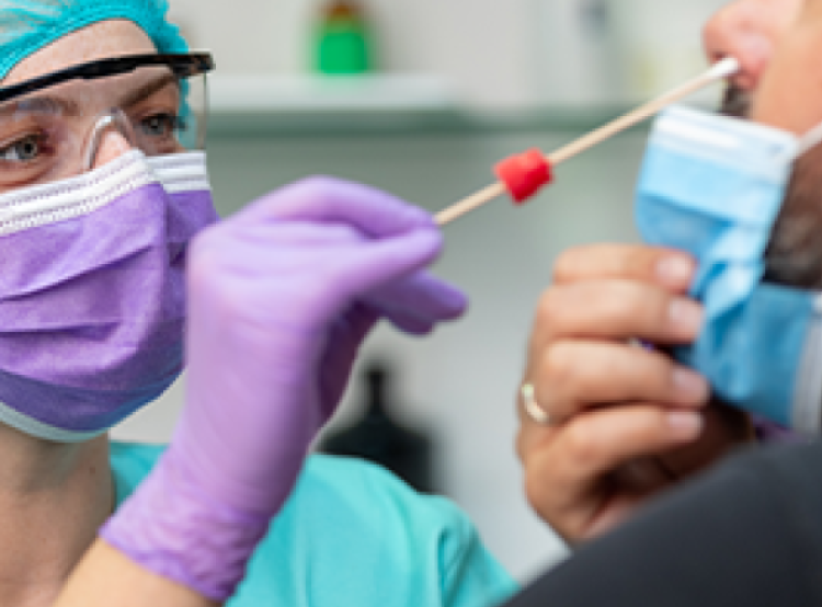 Female nurse in scrubs and face mask performing a COVID-19 test