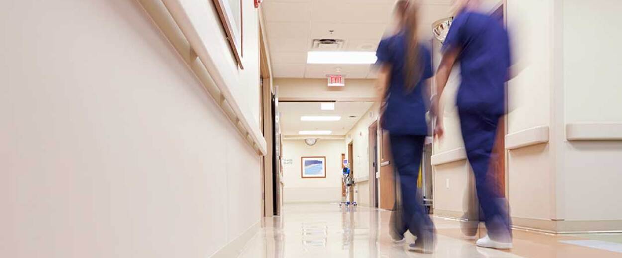 Male and female nurse in scrubs walking down hospital hallway