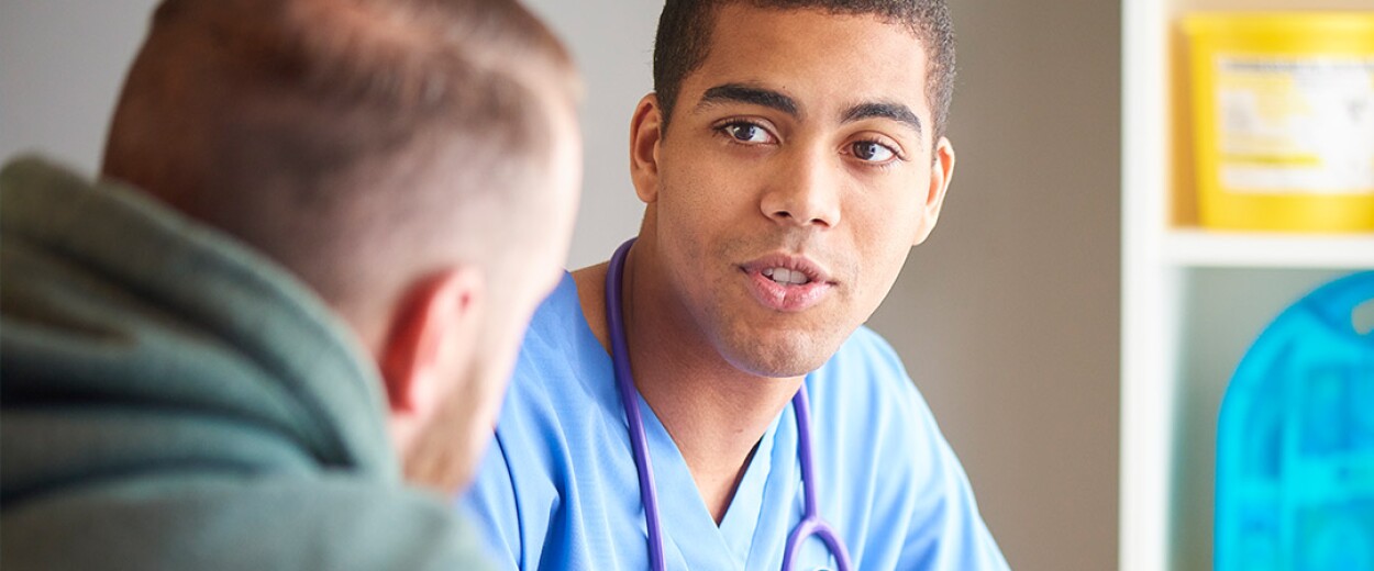 Male nurse in scrubs talking to a male patient