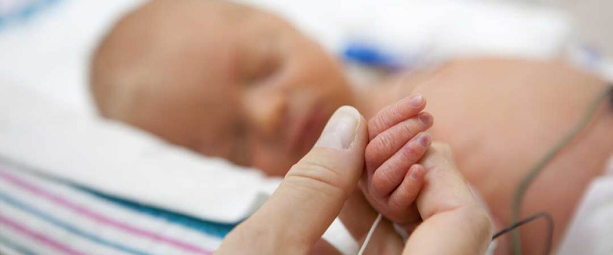 Close-up of NICU nurse holding the hand of a newborn baby