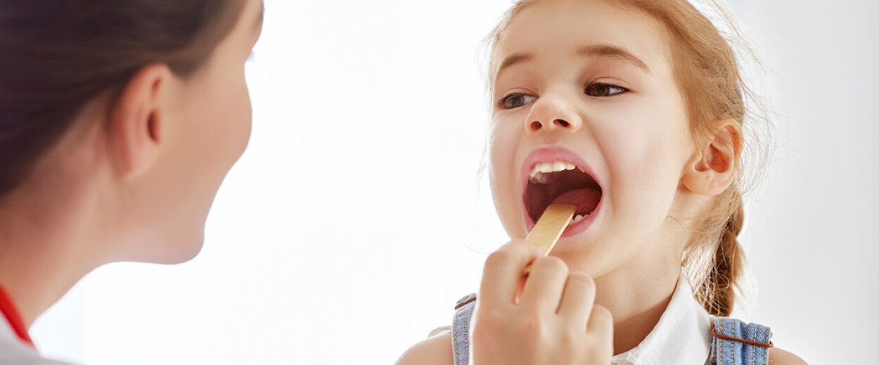 Female nurse looking at small female patient's throat with a tongue compressor