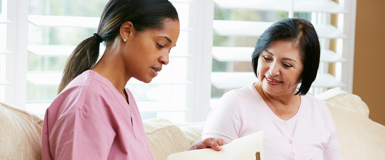 Female nurse in scrubs going over paperwork with a female patient