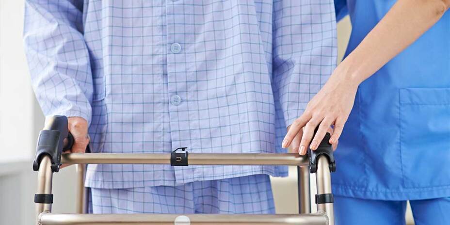 Close up of nurse in scrubs helping elderly male patient in PJs with his walker
